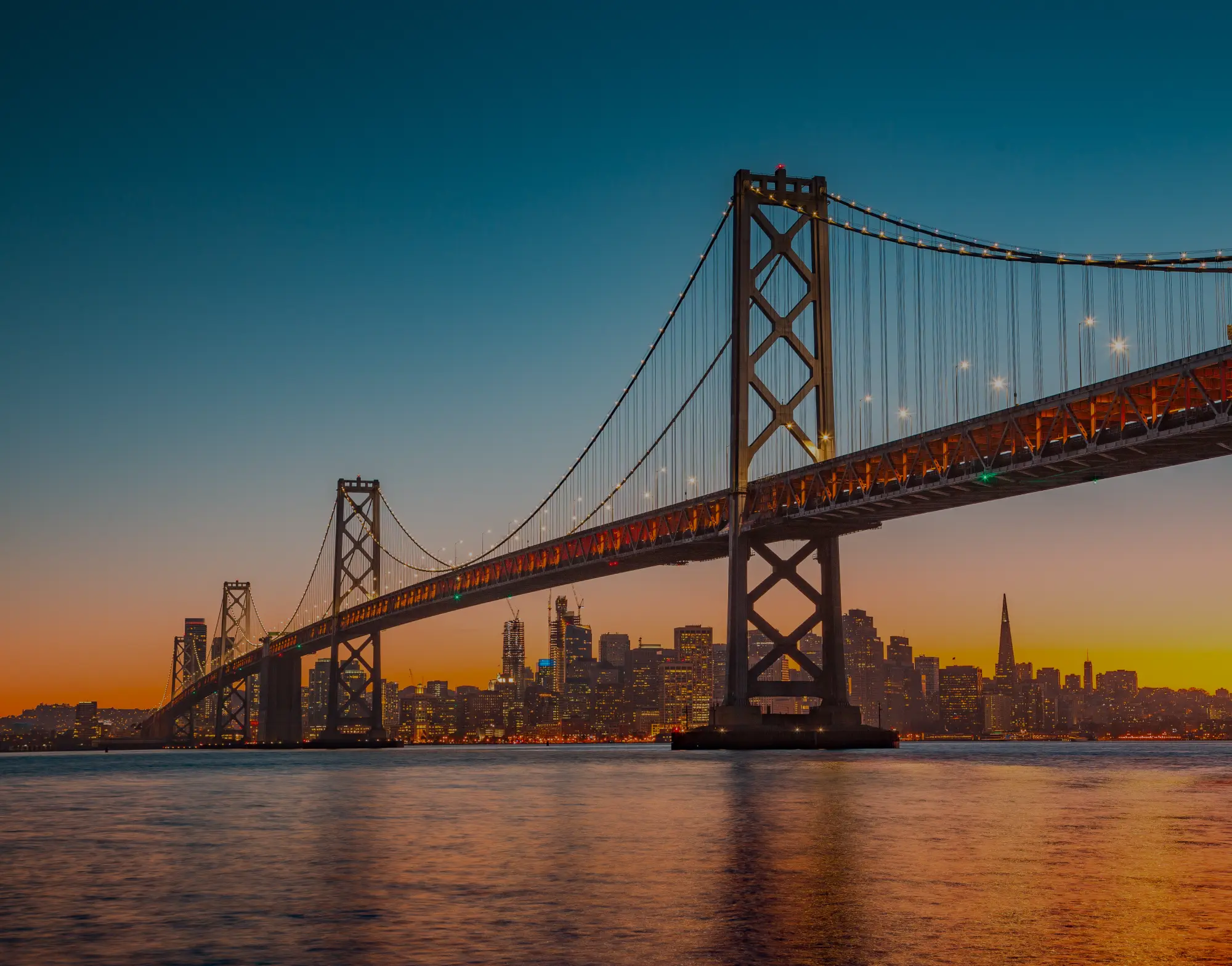Bay Bridge lit at sunset in front of the San Francisco skyline