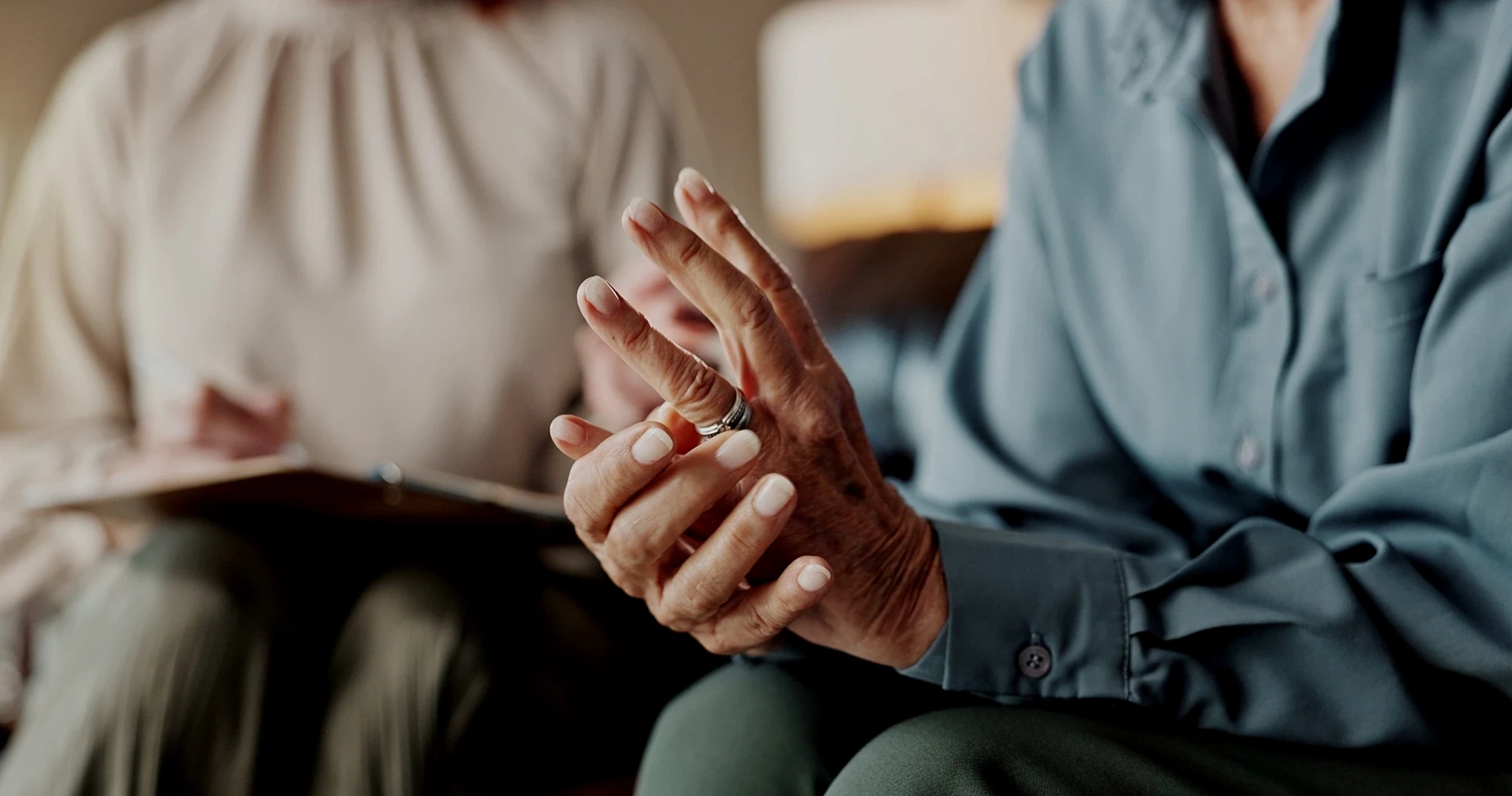 Older couple sitting apart as one twists off a wedding ring