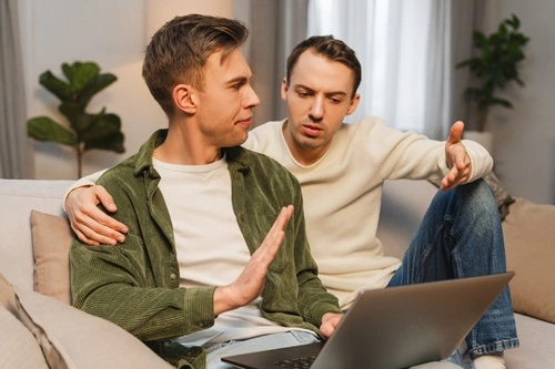 Two men arguing on a sofa over an open laptop