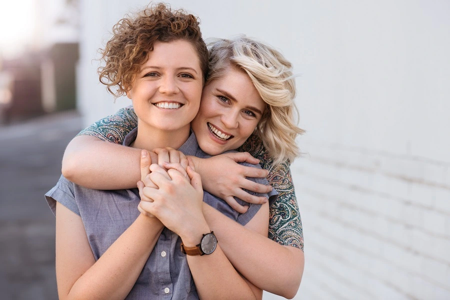 Two smiling women embracing on a sunlit street