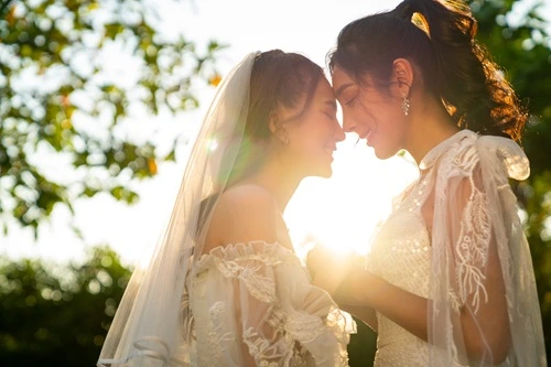 Two brides in wedding dresses touching foreheads at sunset