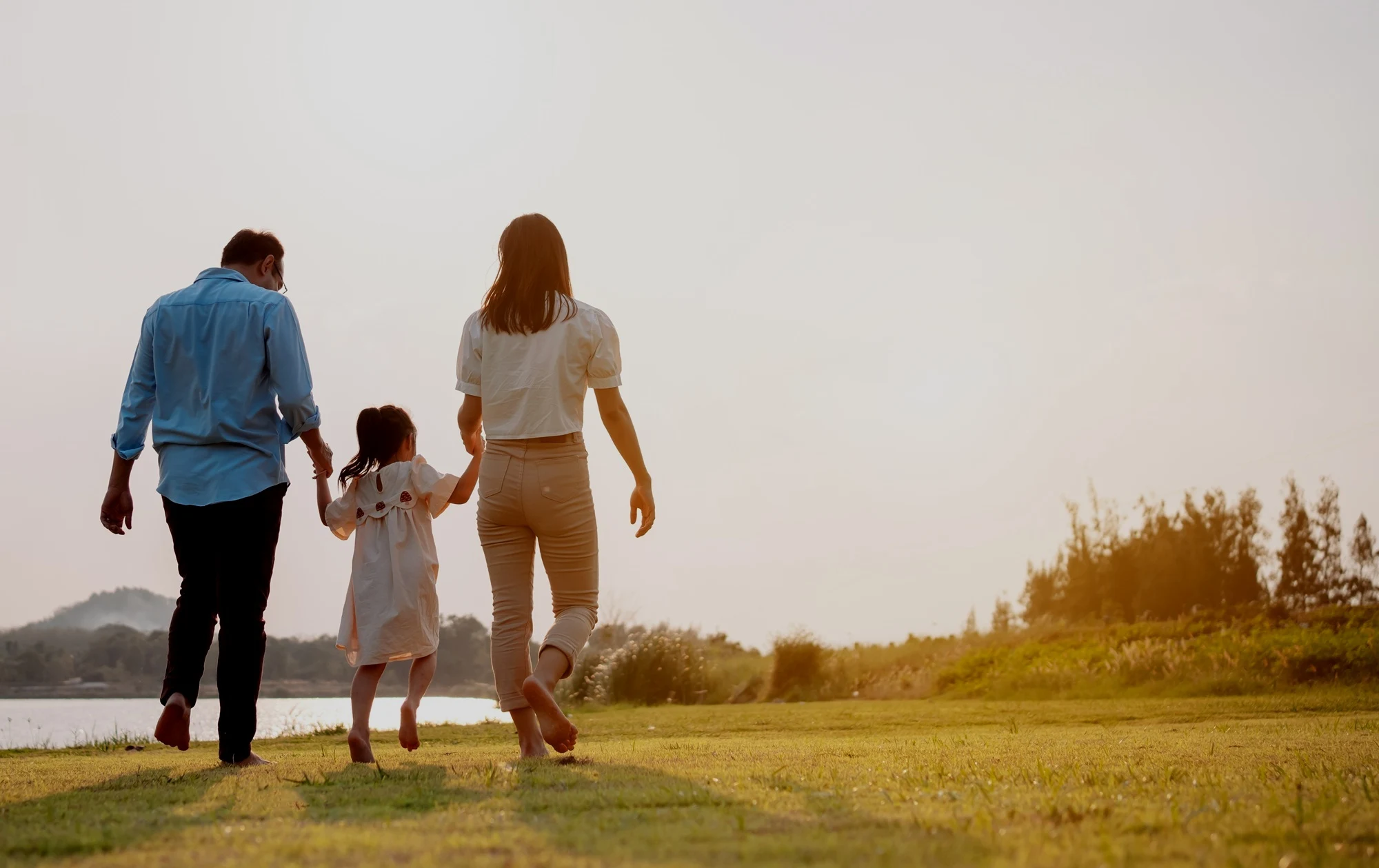 Parents and their young daughter walking hand in hand through a sunlit field