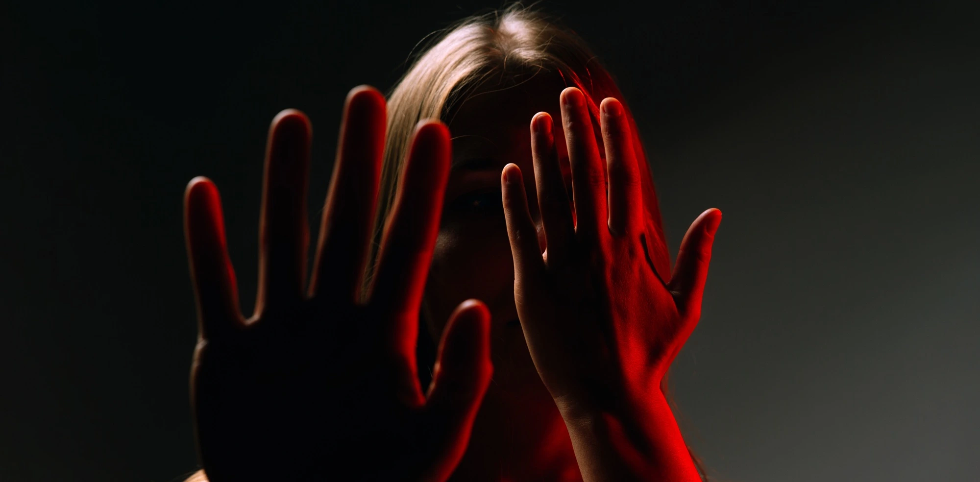 Person raising both hands in defense under harsh red light
