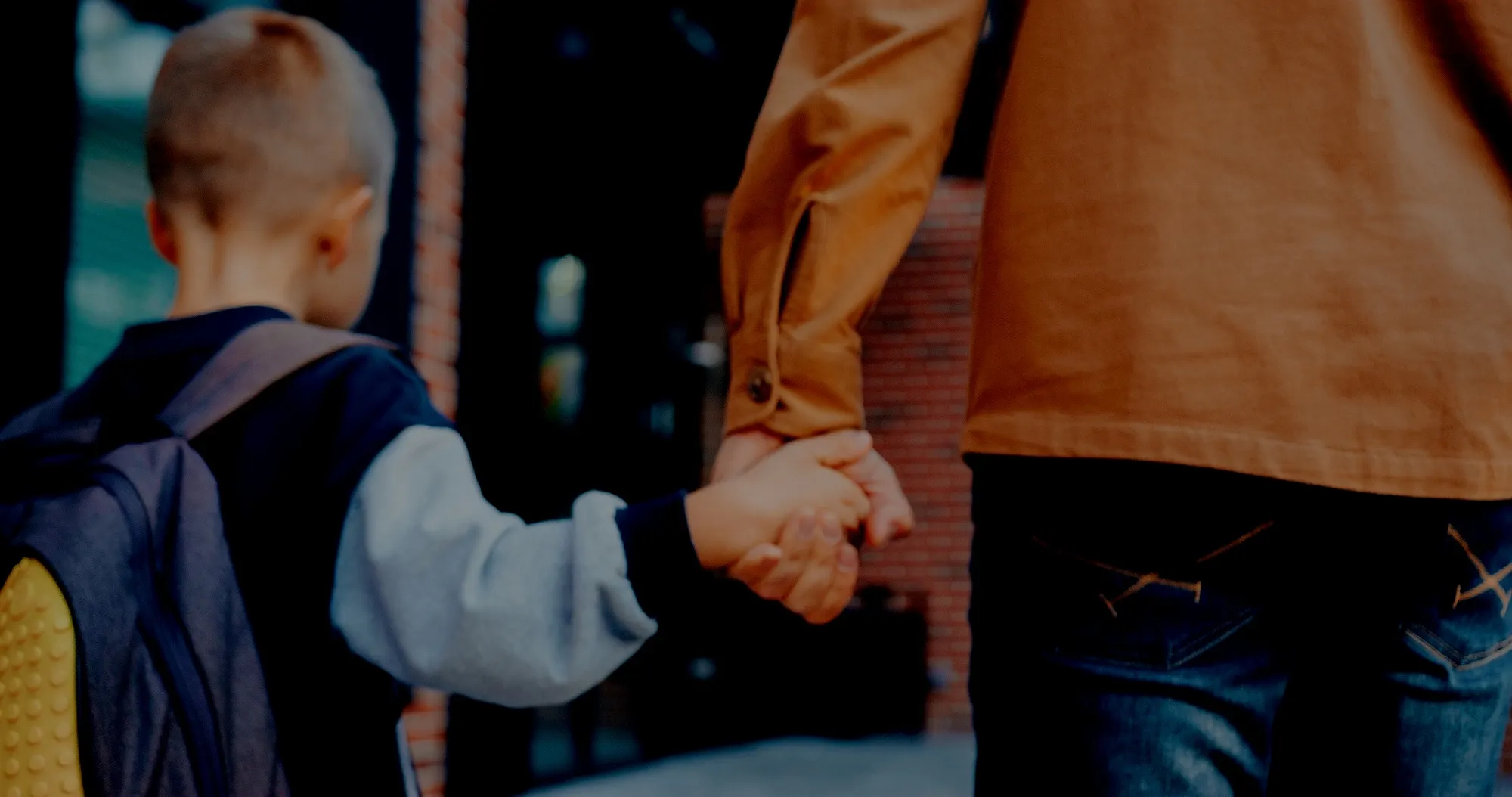 Young child with a backpack holding an adult's hand