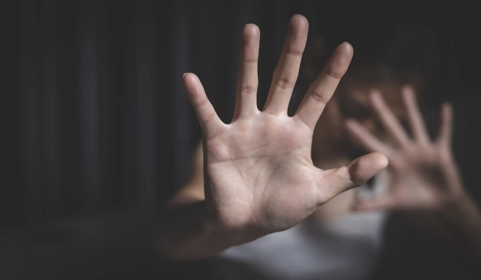 Raised hands signalling stop in a darkened room