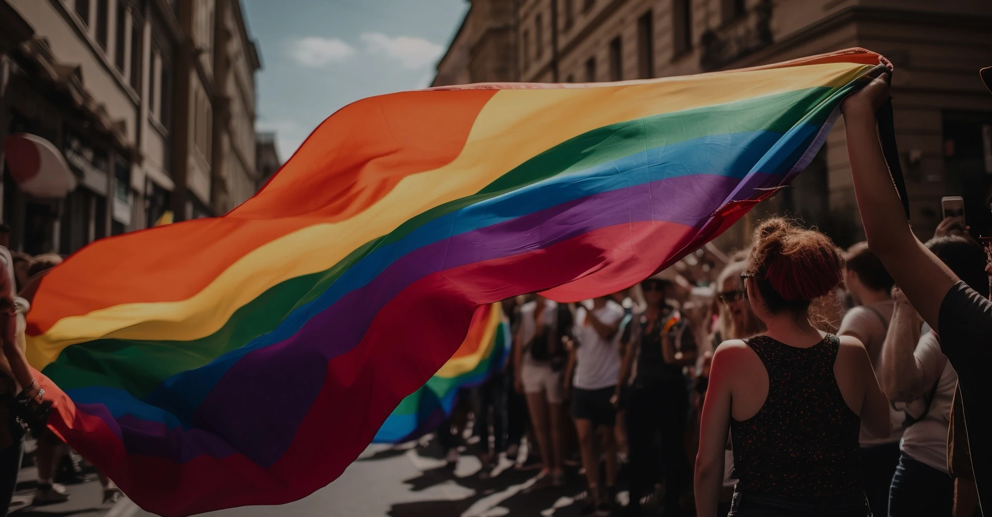 Rainbow pride flag waved above a crowd at a street march