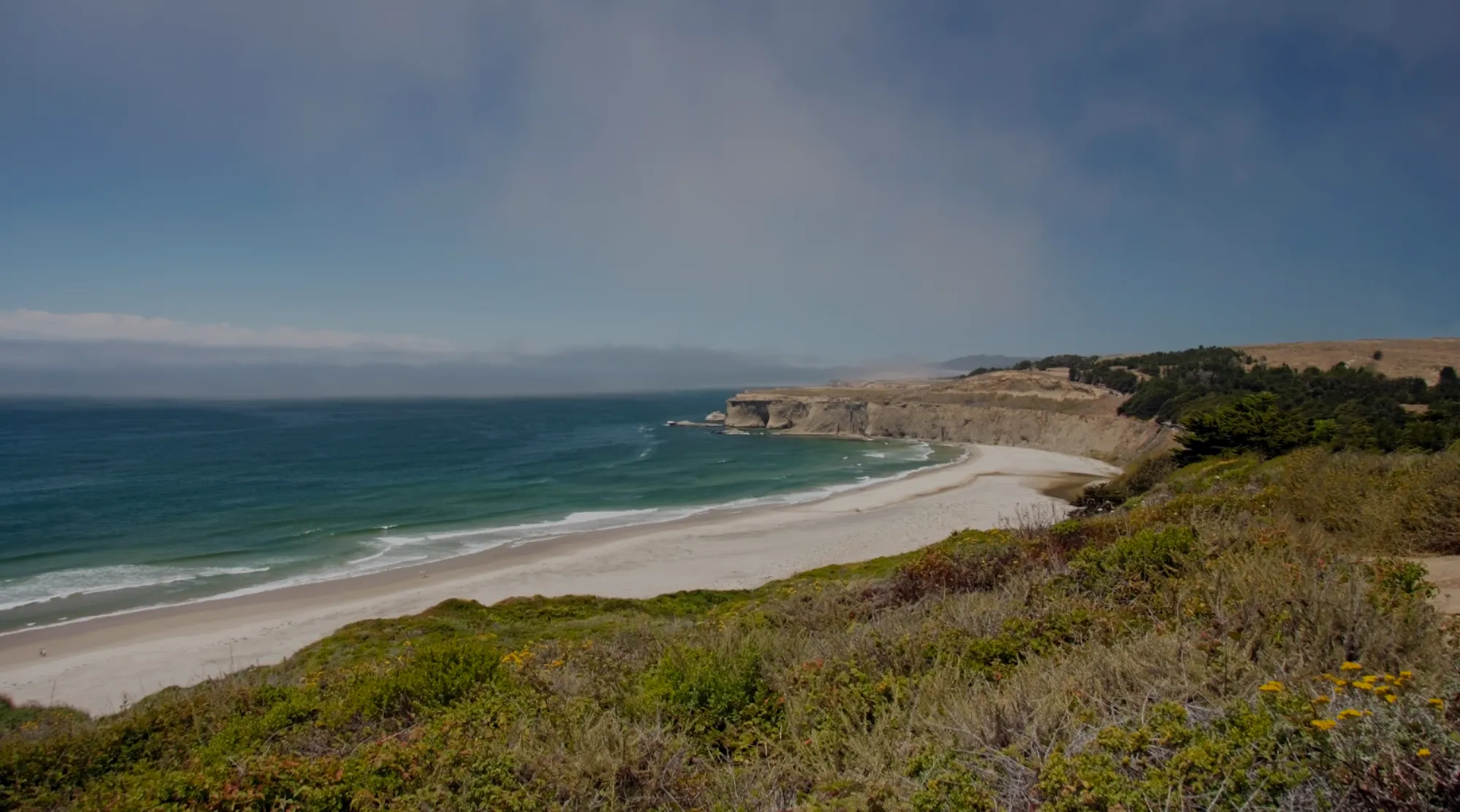 Sandy beach curving below coastal bluffs under a hazy Pacific sky