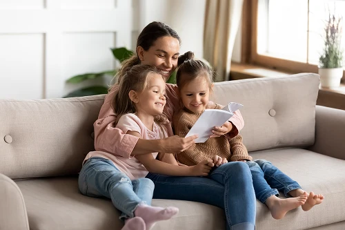 Mother reading a book with her two daughters on a sofa