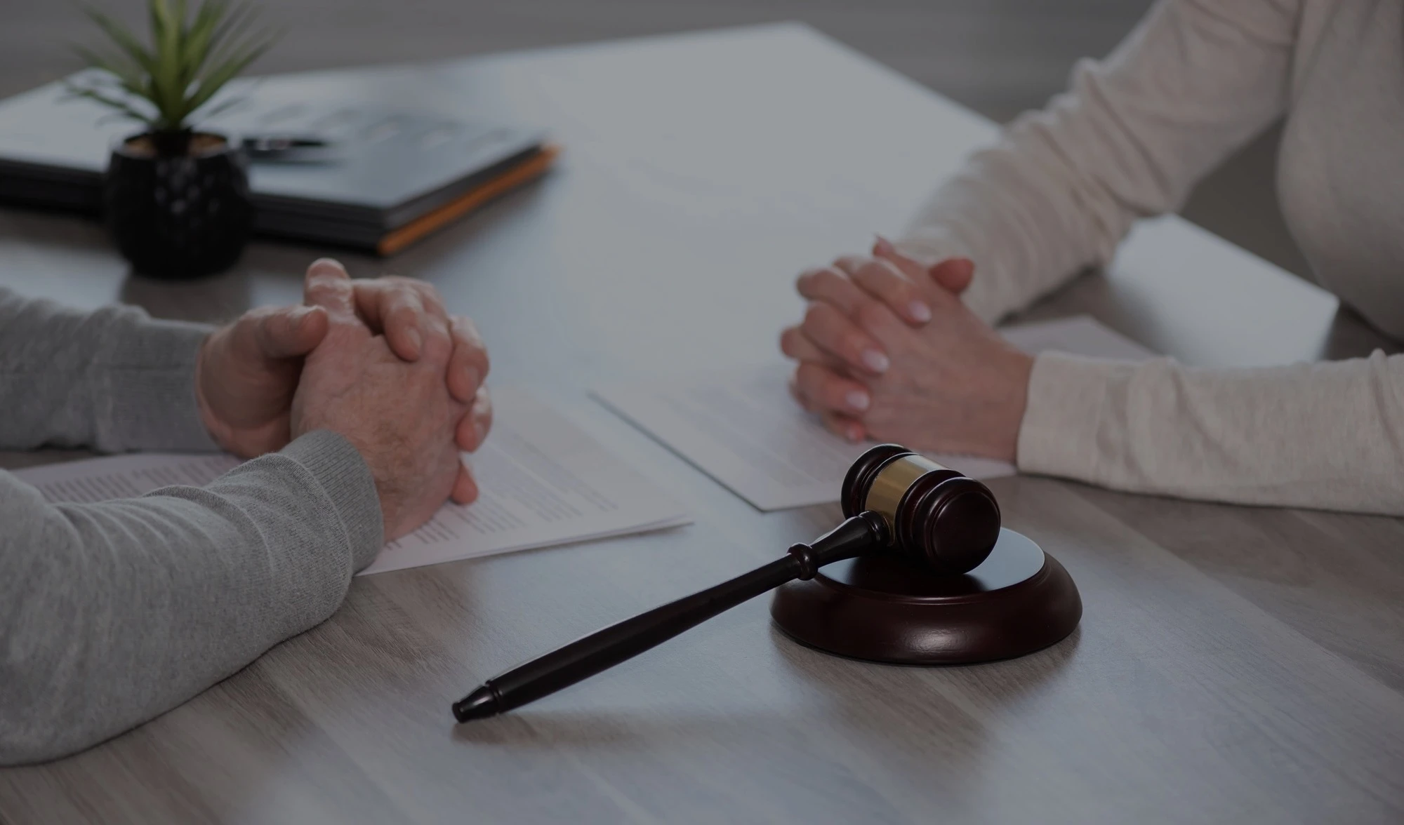 Two people with folded hands at a table with a gavel and papers