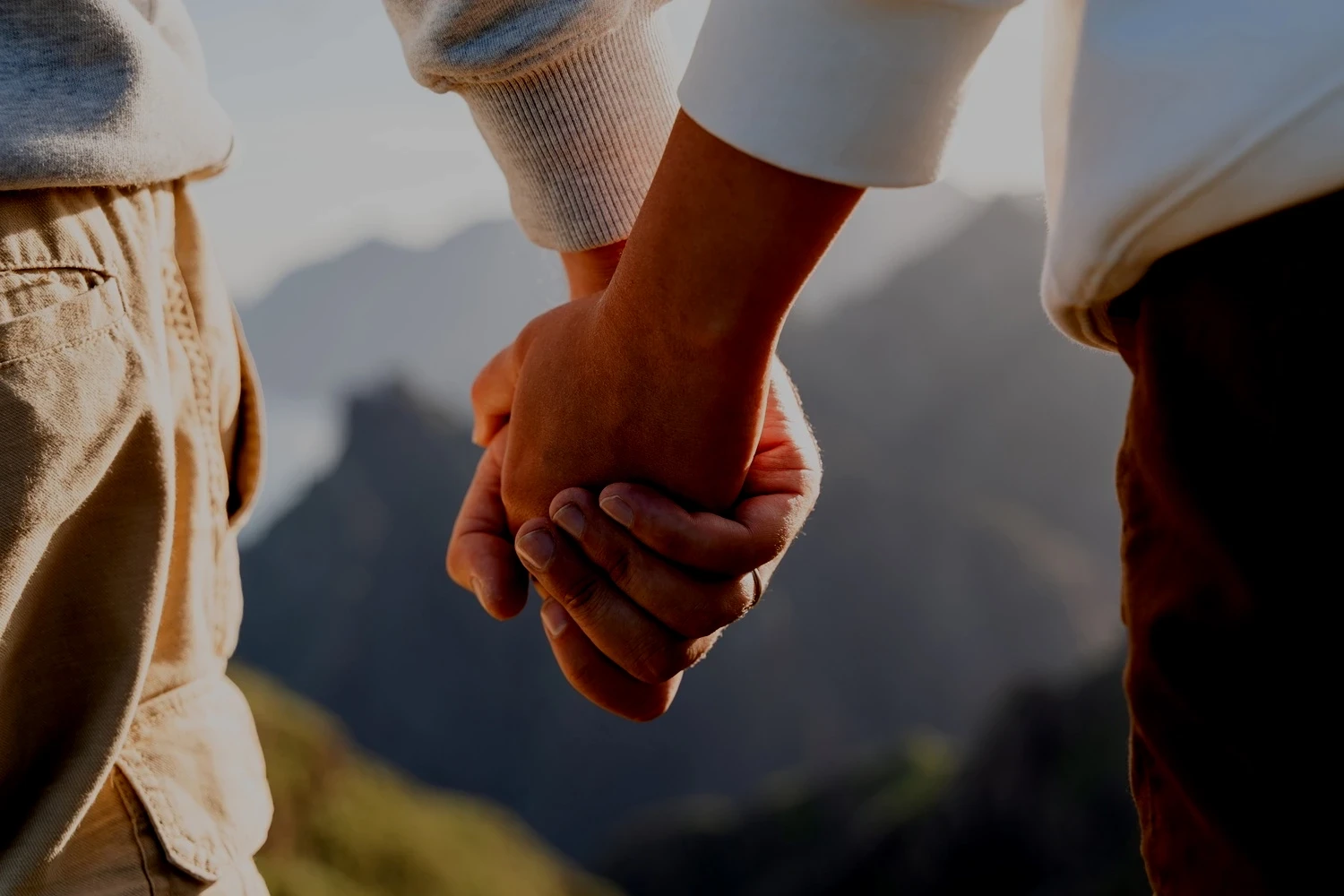 Two people holding hands outdoors with wedding bands visible