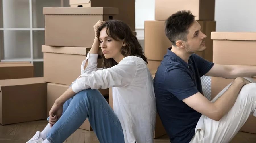 Couple sitting back to back among packed moving boxes