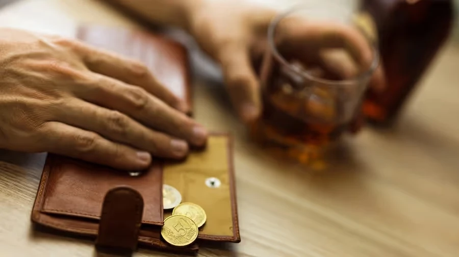 Hand resting on a wallet of coins beside a whiskey glass