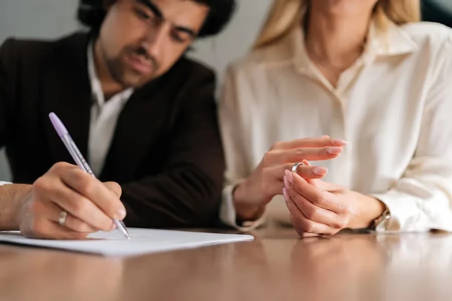 Woman removing her wedding ring as a man signs a document