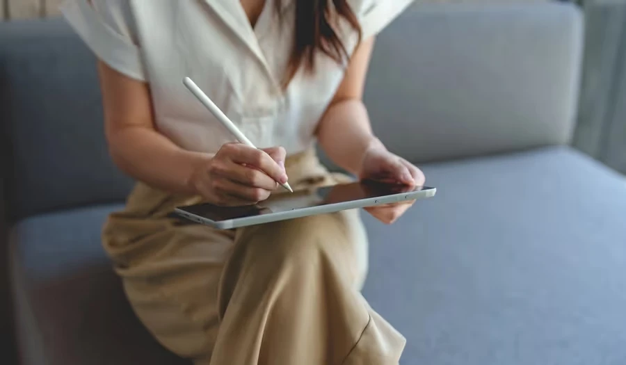 Woman writing on a tablet with a stylus on a sofa