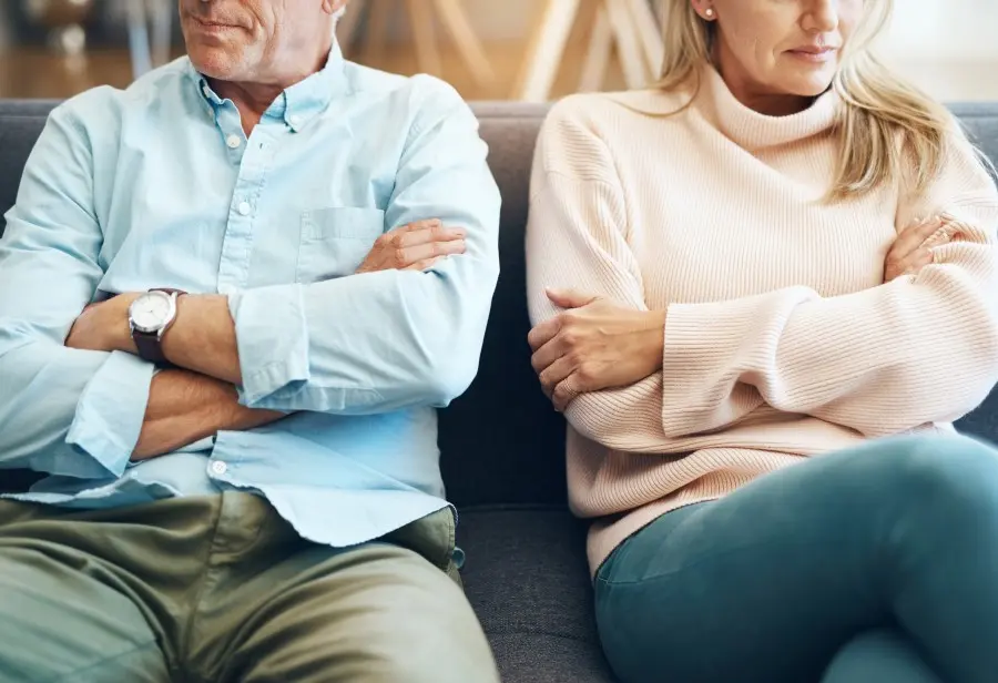 Older couple sitting apart on a sofa with arms folded