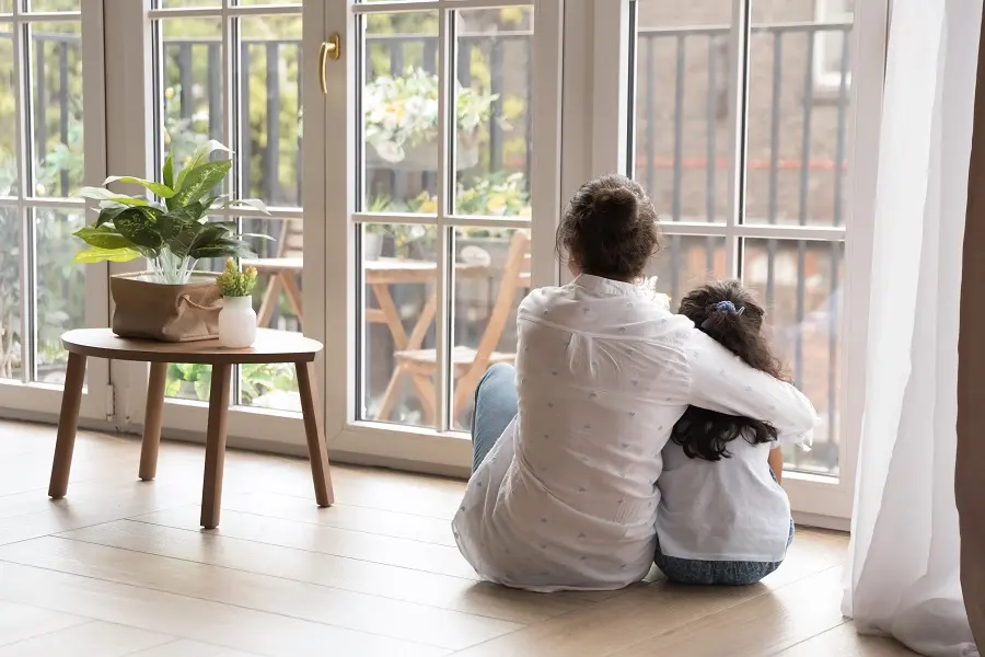 Mother and daughter sitting on the floor by a window, holding each other