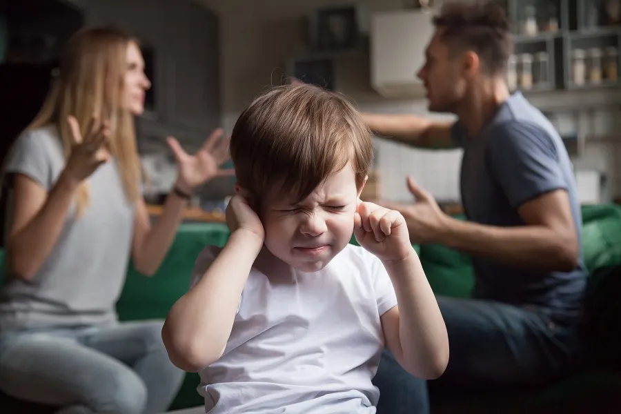 Boy covering his ears while his parents argue behind him
