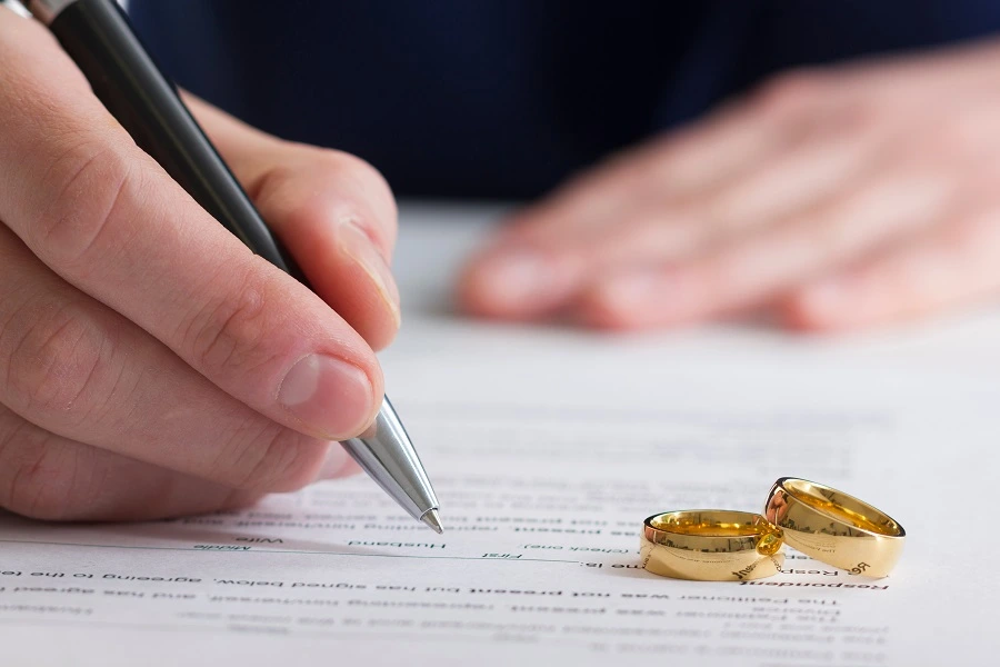 Hand signing a document beside two wedding rings